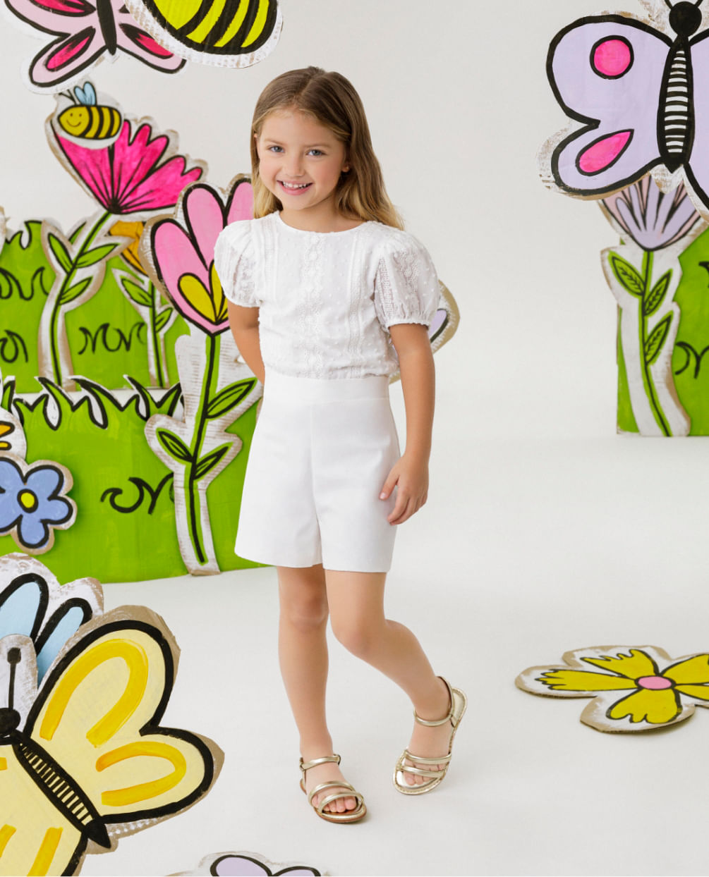 Foto de modelo niña usando blusa manga corta color blanco, short blanco y sandalias planas color dorado