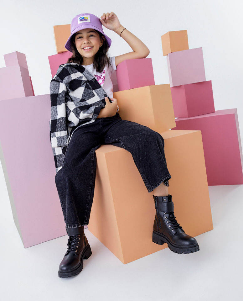 Foto de niña usando bucket hat morado, camiseta blanca, chaqueta de cuadros, jean para niña y botas ELA